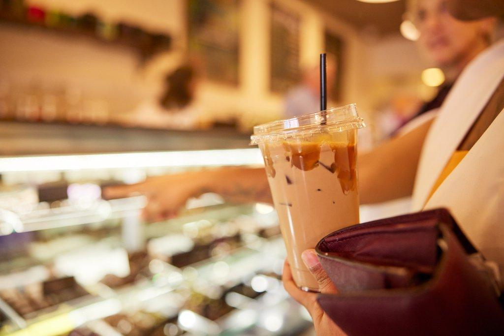 Customer holding an iced beverage looking at a counter case of sweet treats.